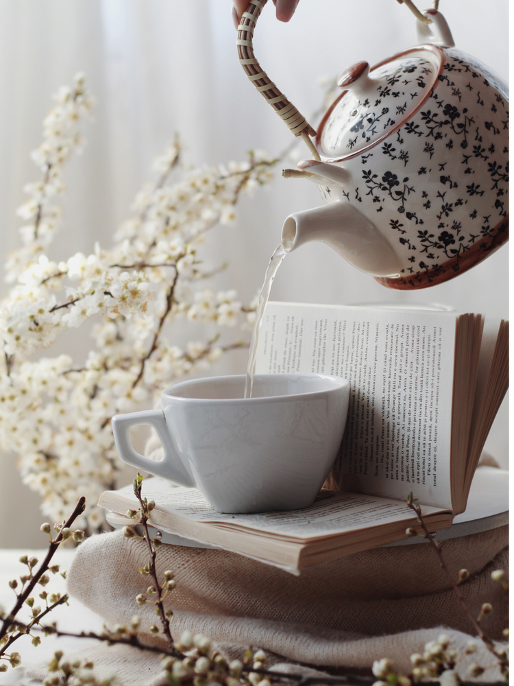Morning tea ritual with tea pot and ceramic cup and book with dried florals.