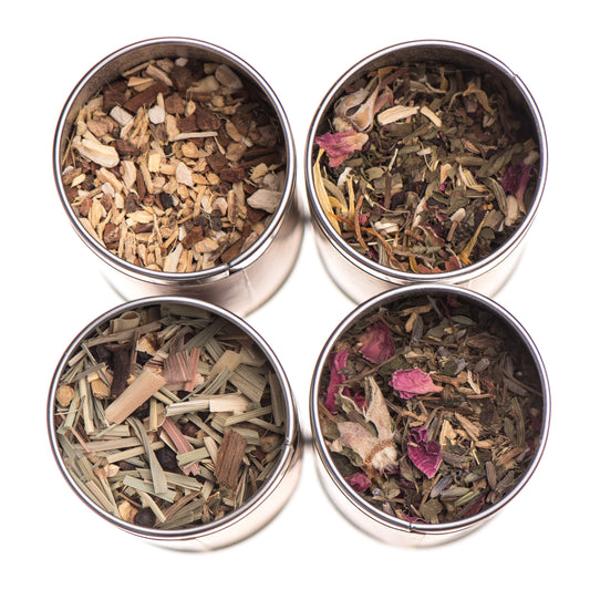 Four metal tins filled with different types of dried herbs and teas on a white background