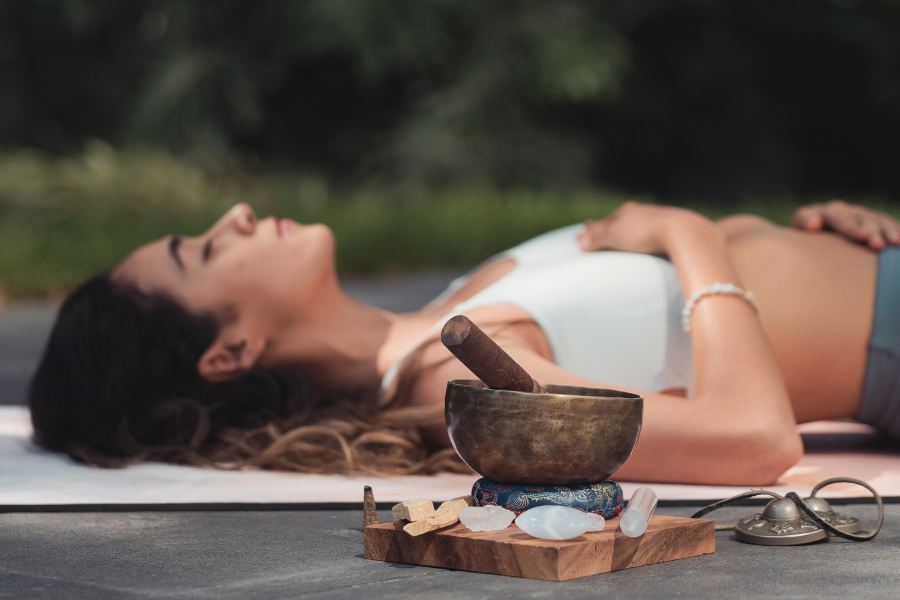 Woman lying on a mat with a meditation bowl and stones in the foreground